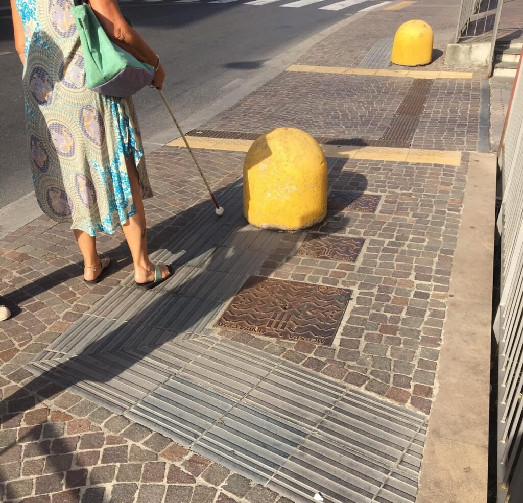 A bollard placed in the middle of a tactile paving path, an architectural barrier