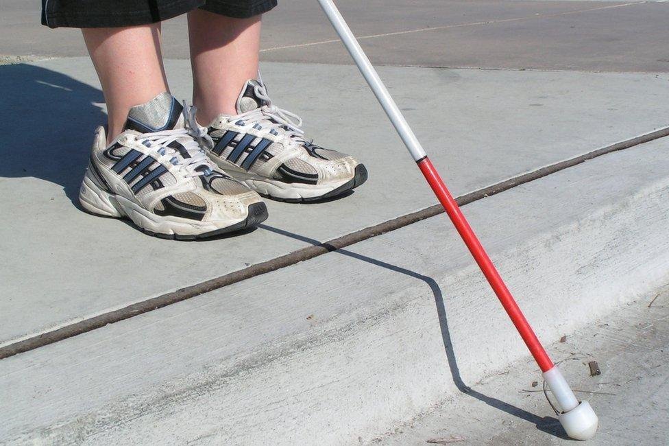 Feet and a white cane following a tactile paving guide path